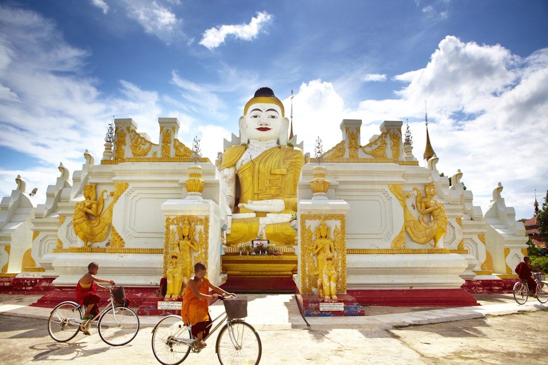 Novice monks cycling past 26-foot high sitting Buddha at Yan Aung Nan Aung Hsu Taung Pyi Pagoda near Inle Lake.