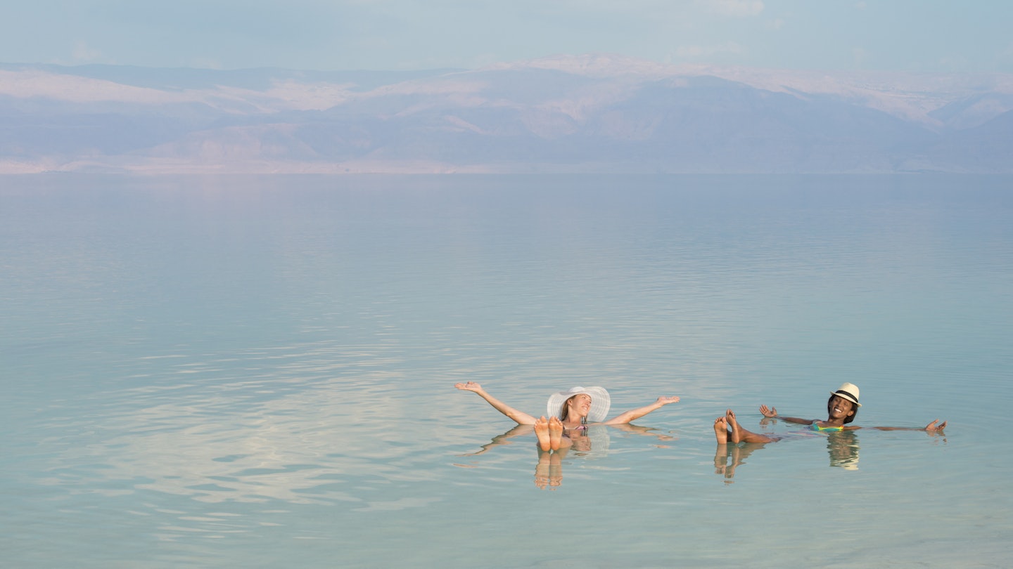 Lovely girls floating in salty water of Dead Sea and with Arms outstretched . Unusual buoyancy caused by high salinity.