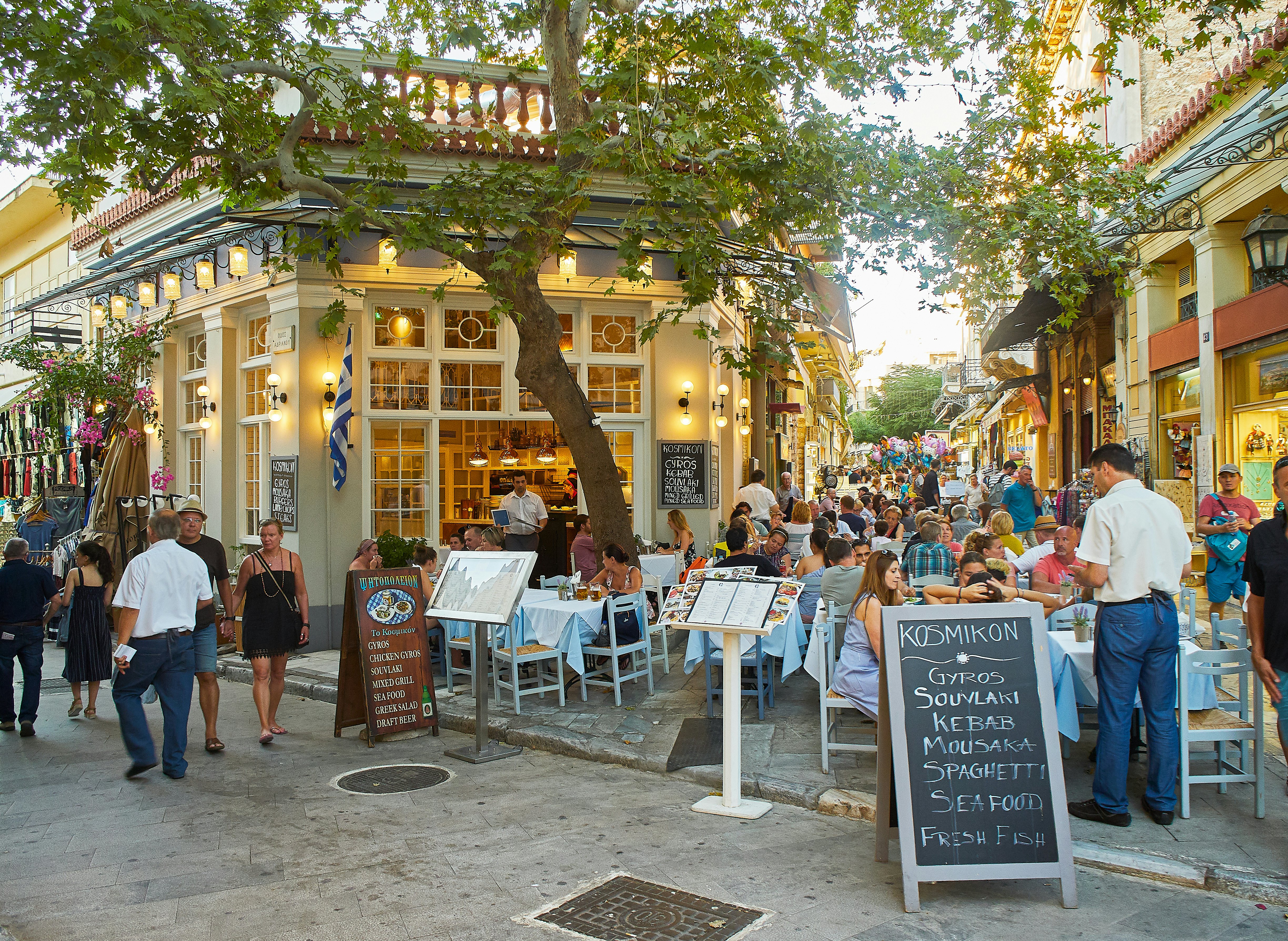 People dining at a terrace of a Greek restaurant in a busy city neighborhood