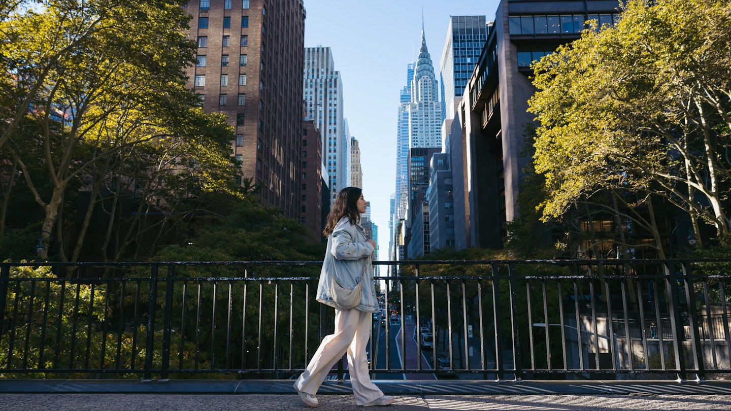 Side view of a young woman wearing an oversized denim jacket walking on the Tudor City Bridge, New York.