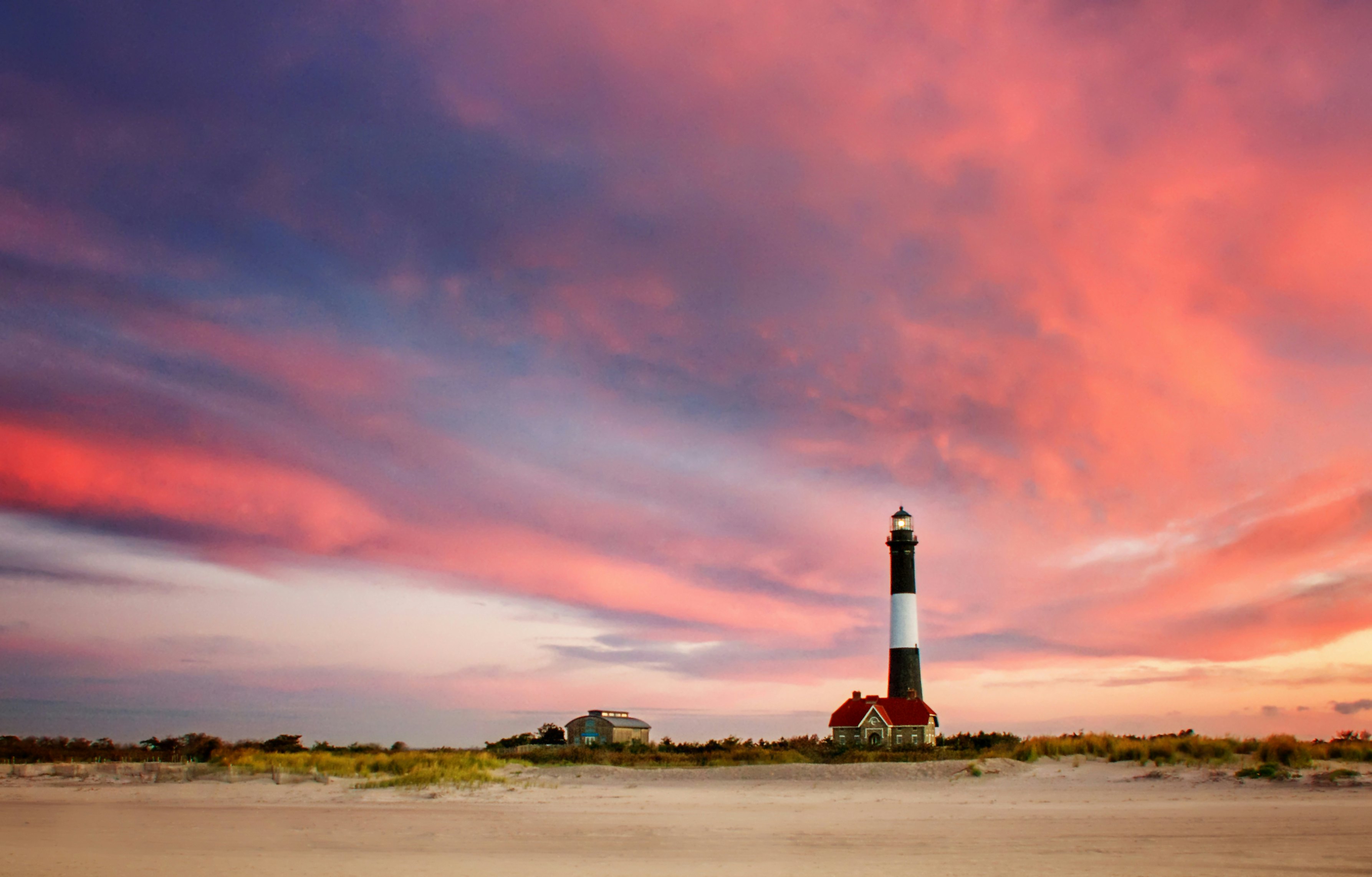 Early morning clouds light up in pink and magenta against a blue sky at the Fire Island Lighthouse, Kismet, Long Island, as seen from the Lighthouse beach.
