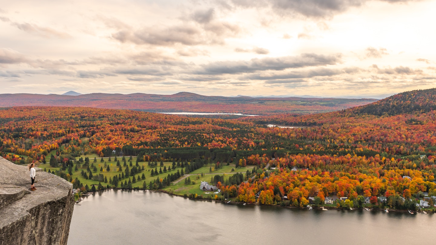 Woman looking at Lyster lake with forest of Quebec and Vermont seen from the Mount Pinacle in Coaticook during autumn.