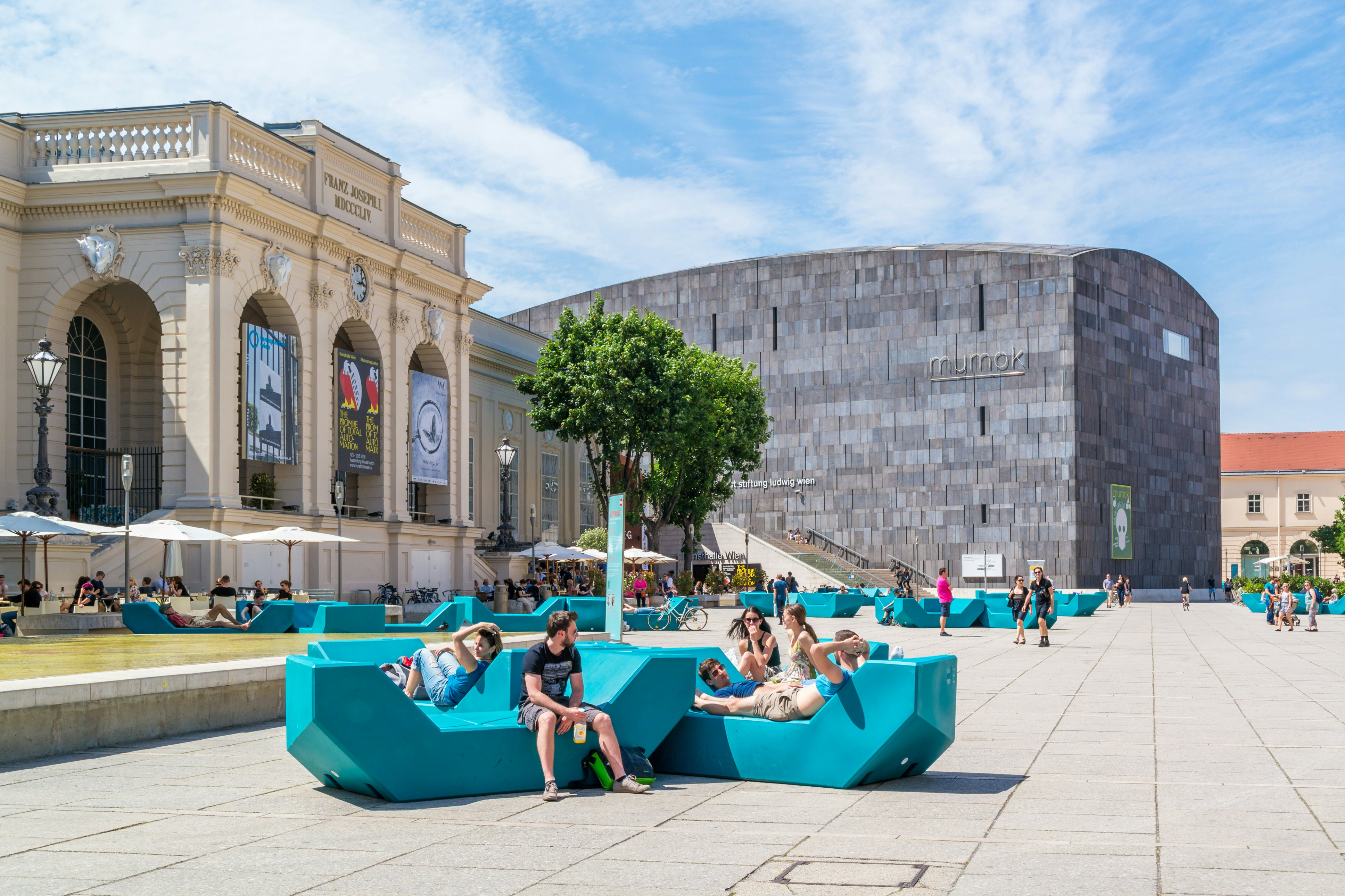 People relax in the sunshine on angular seats in a public square