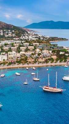 Boats float on bright blue water along a coastline covered in buildings.