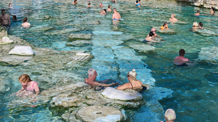 A group of people swim in a thermal spring with clear blue water.