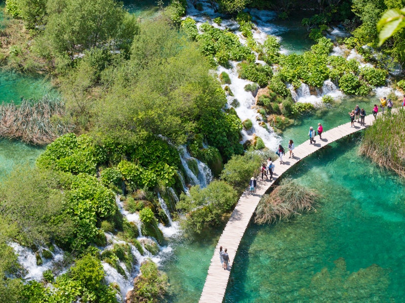 People walk along the boardwalk in front of waterfalls in Plitvice national park.