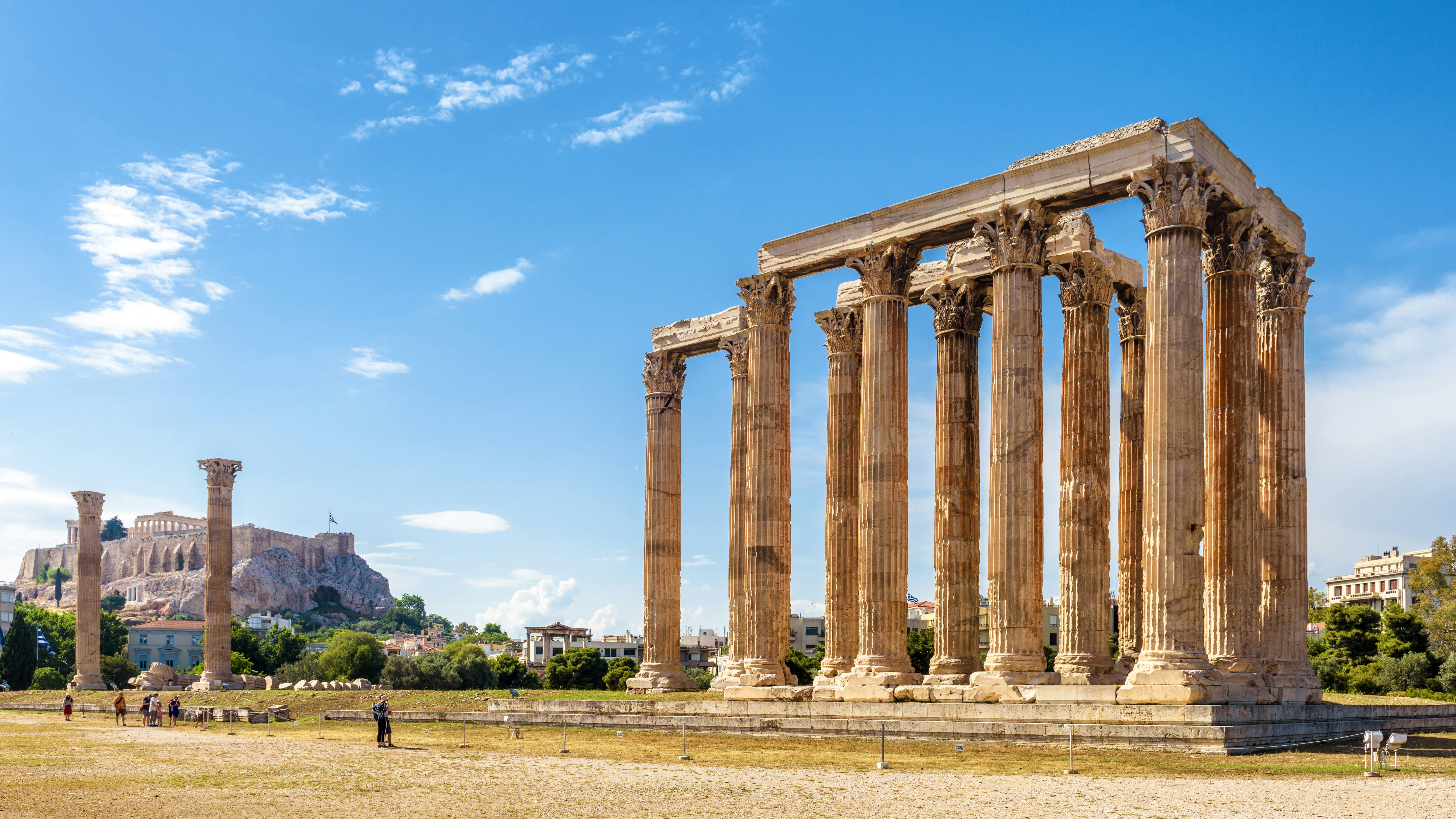 Huge ancient columns are seen at an archeological site, with people looking on.