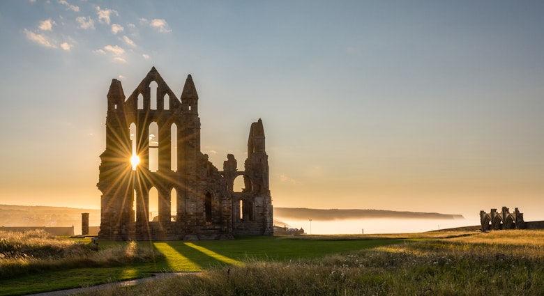 Sun Star on Whitby Abbey / The Gothic ruins of Whitby Abbey with the suns rays producing a star. Sea mist held back by the cliffs at Sandsend in the background, License Type: media, Download Time: 2024-12-18T22:11:25.000Z, User: meg3348277, Editorial: false, purchase_order: 56530 - Guidebooks, job: Global Publishing-WIP, client: England 13, other: Megan Cassidy