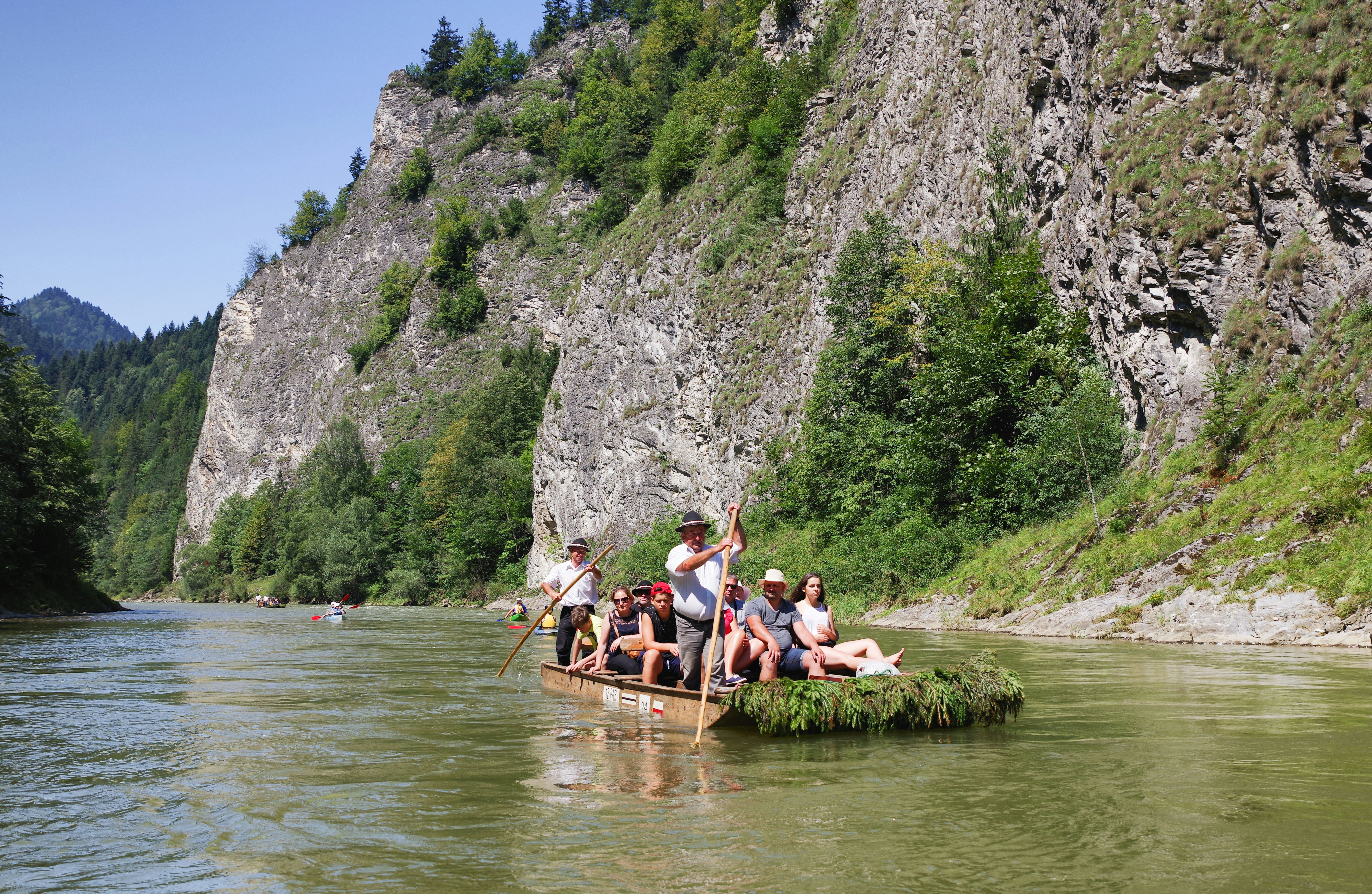 Men in traditional costumes navigate a raft with passengers in a mountain river.