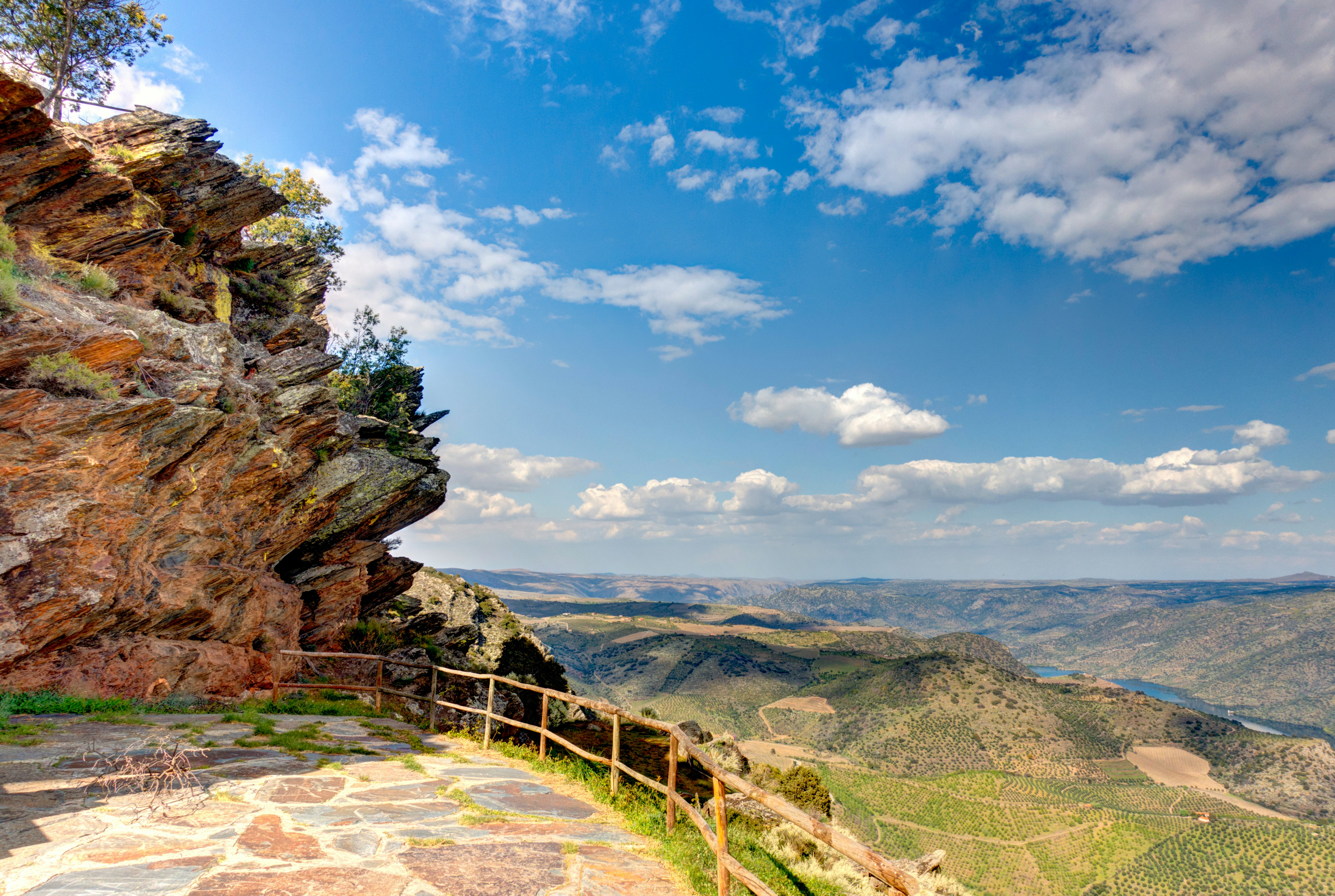 A large rocky outcrop casts shade over viewpoint with a view stretching out across an undulating river valley
