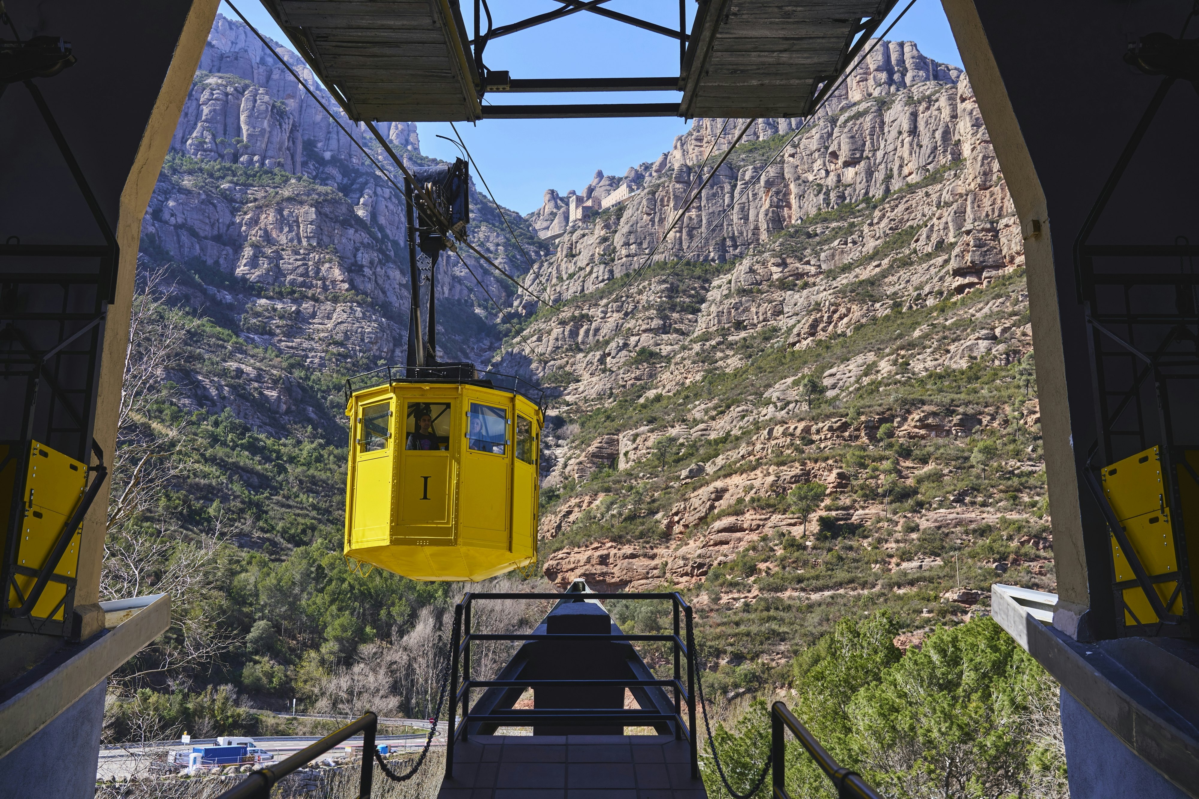 Low angle view of a yellow cable car arriving at station against rock cliff of Montserrat Mountain